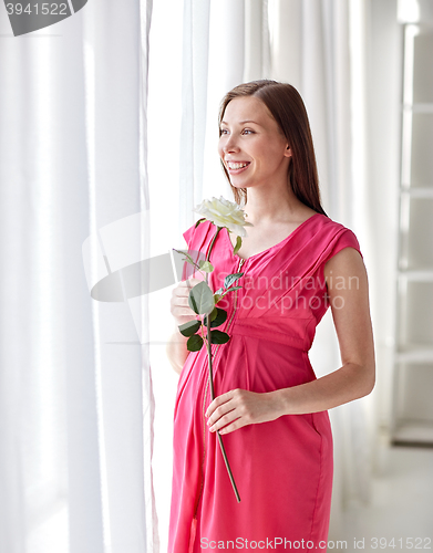 Image of happy pregnant woman with rose flower at home