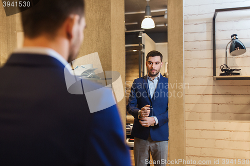 Image of man trying jacket on at mirror in clothing store