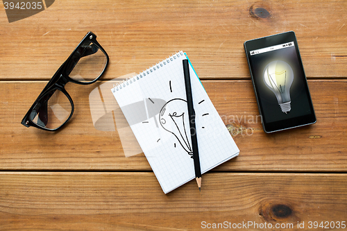 Image of close up of notepad, smartphone and eyeglasses