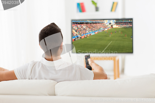 Image of man watching football or soccer game on tv at home