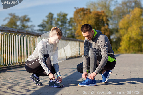 Image of smiling couple tying shoelaces outdoors