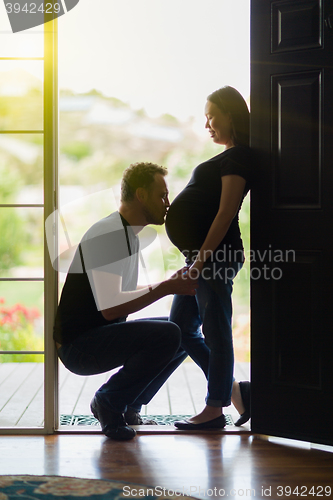 Image of Husband Kissing Belly of Pregnant Wife In Doorway.