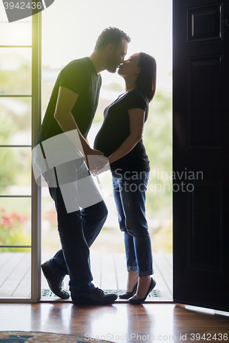 Image of Mixed Race Pregnant Couple Kissing in Doorway.