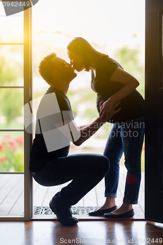 Image of Mixed Race Pregnant Couple Kissing in Doorway.