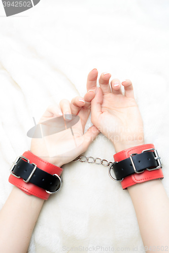 Image of female hands in leather handcuffs. on the background sheet. sex toys.