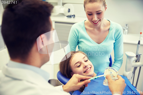 Image of happy dentist showing toothbrush to patient girl