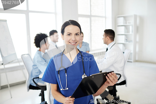 Image of happy doctor with clipboard over group of medics