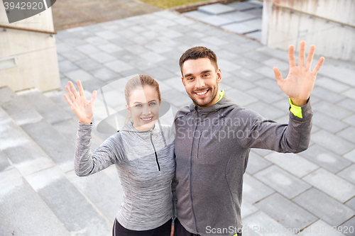 Image of happy couple waving hands outdoors on city street