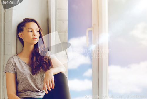 Image of sad pretty teenage girl sitting on windowsill