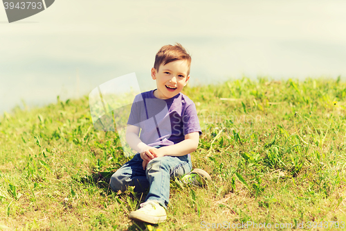 Image of happy little boy sitting on grass outdoors