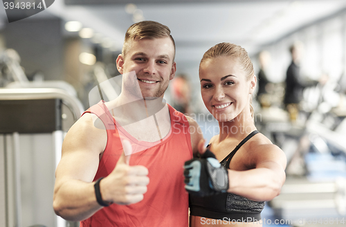 Image of smiling man and woman showing thumbs up in gym