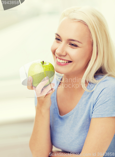 Image of happy woman eating green apple at home