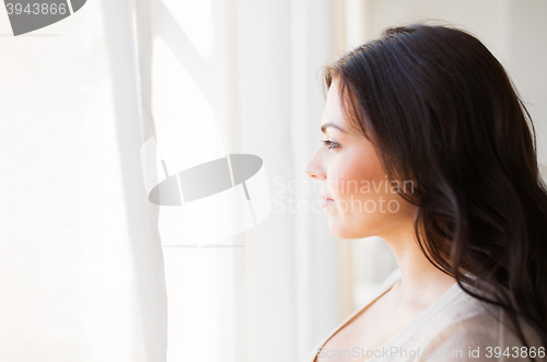 Image of young woman looking through window at home