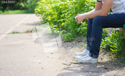 Image of Young man sitting wearing jeans outdoor.