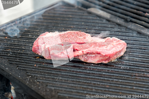 Image of raw steak with spices on metal grill