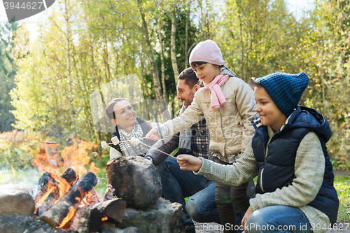 Image of happy family roasting marshmallow over campfire