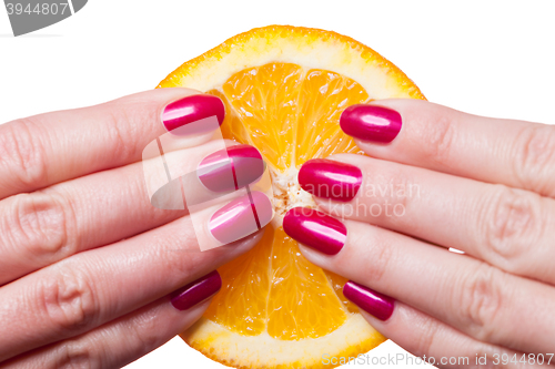 Image of Hand with manicured nails touch an orange on white