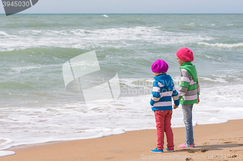 Image of Two girls holding hands standing on the beach and looking into the distance