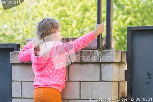 Image of Five-year girl climbed on a brick fence and looks for him