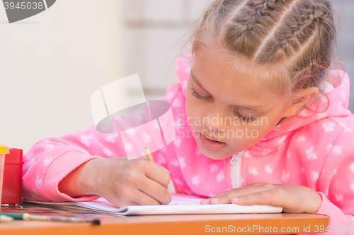 Image of Schoolgirl is drawing in pencil on the album, in the yard