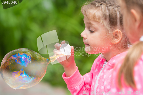 Image of Five-year girl inflates a large bubble, another girl with interest looks at her