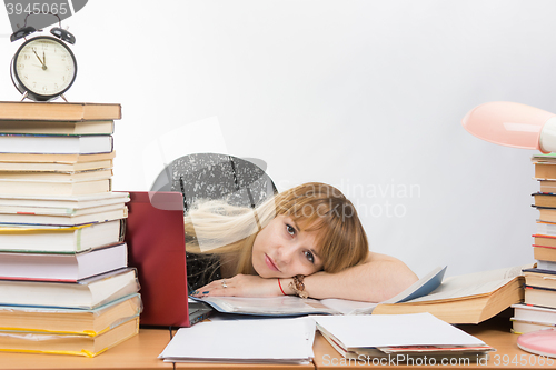 Image of Girl student lay behind a desk crammed with books and papers