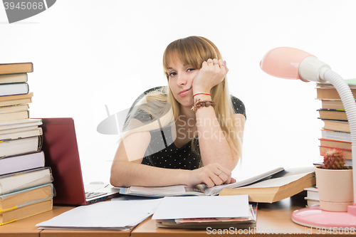 Image of Student sadly sitting at a table among the stacks of books and papers