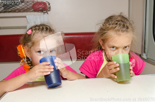 Image of Two children drink tea in train at the table on the lower place in the second-class compartment wagon