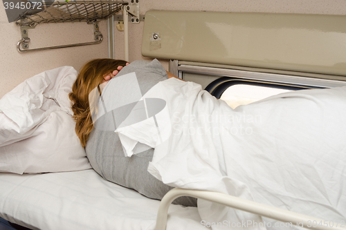 Image of The girl sleeps on the top shelf of the side seats in the second-class carriage turned to the wall