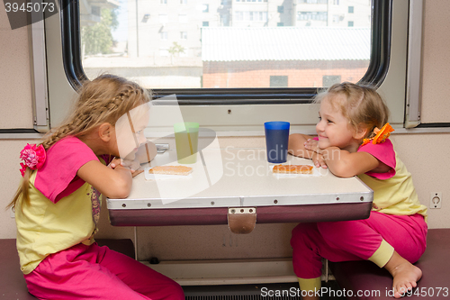 Image of Two little girls with a happy face looking at each other on the train sitting at the table on outboard second-class carriage