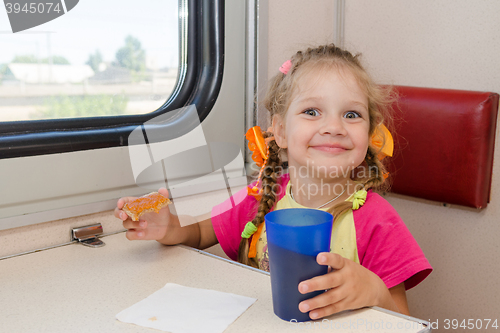 Image of Little girl with a happy face drink tea with a sandwich on the train at the table on outboard second-class carriage