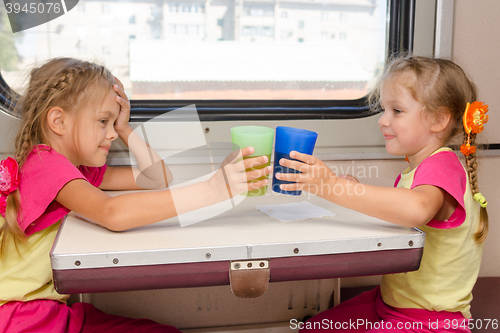 Image of Two little sisters in identical pajamas drinking tea in the train at the table on outboard second-class carriage