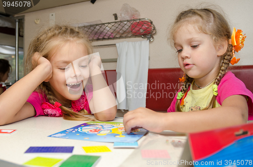 Image of Two girls having fun playing on the train at the table on the lower place in the second-class compartment wagon