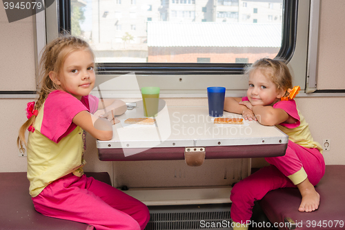 Image of Two little girls on the train sitting at the table in the outboard second-class car in the same clothes