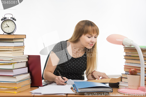 Image of Pretty female student at a table littered with books in the library writing job