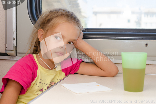 Image of Six-year girl thoughtfully and tired sitting on the train at the table in the second-class compartment