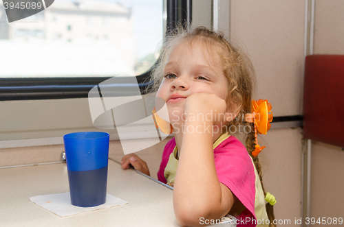 Image of A girl of four years of thoughtful and tired of sitting on the train at the table on the side a place reserved seat