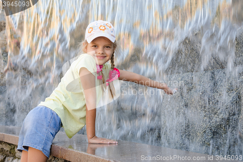 Image of Girl in summer clothes with a smile stretching his hand to water the artificial waterfall