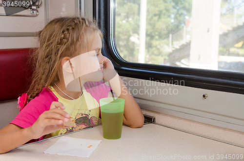 Image of Six-year girl sitting on the train at the table on outboard second-class carriage and enthusiastically looking out the window