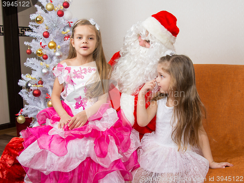 Image of The older girl is sitting on the lap of Santa Claus and tells poem
