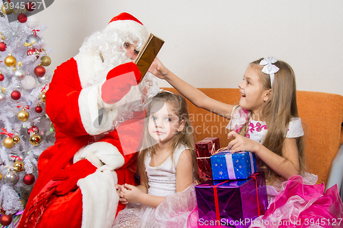 Image of Santa Claus gives gifts to one girl, the other sitting in the waiting