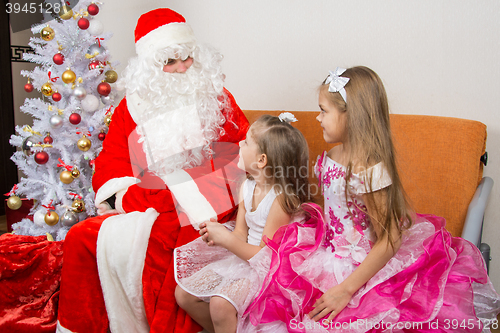 Image of Two girls in beautiful dresses talk with Santa Claus