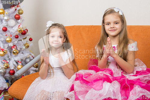 Image of Two girls in beautiful dresses guessing gifts for the new year