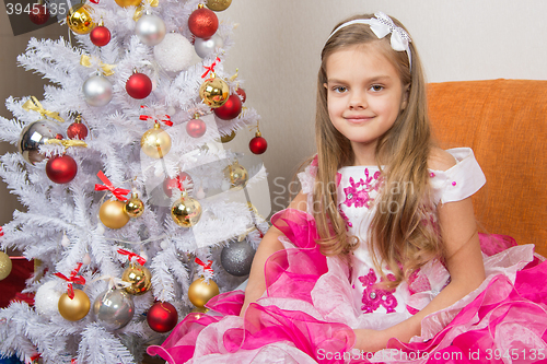 Image of Seven-year girl sitting on a sofa in a beautiful dress the Christmas tree