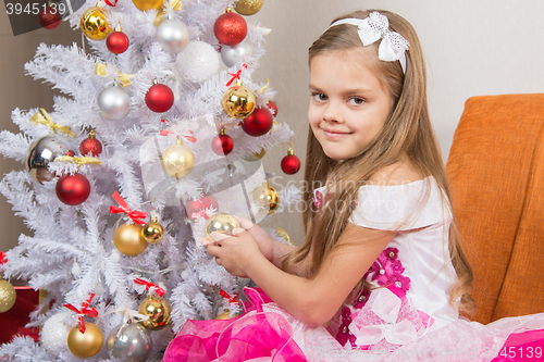 Image of Seven-year girl in a beautiful dress treats Christmas toys and looked into the frame