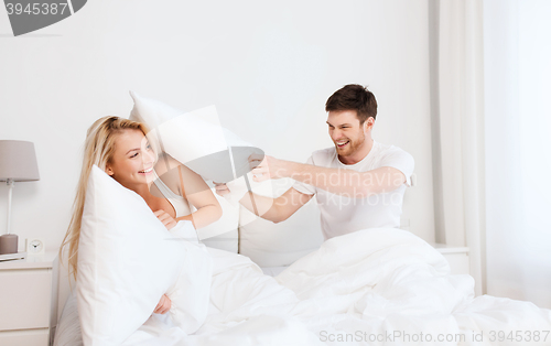 Image of happy couple having pillow fight in bed at home