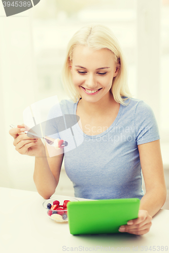 Image of smiling woman eating fruits with tablet pc at home