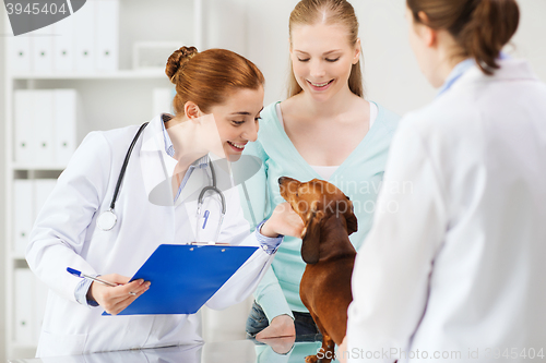 Image of happy woman with dog and doctor at vet clinic