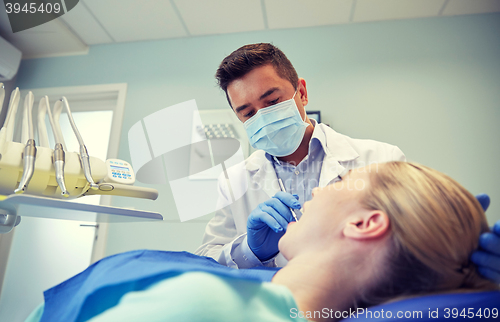 Image of male dentist in mask checking female patient teeth