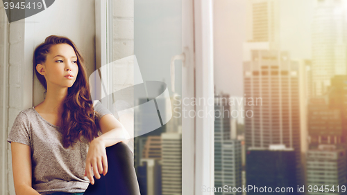 Image of sad pretty teenage girl sitting on windowsill